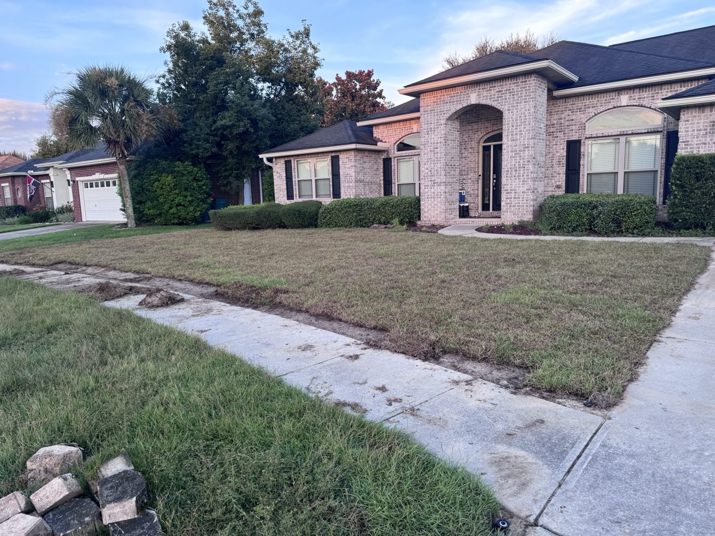 A strip of fresh green sod laid along a concrete sidewalk in front of a brick-fronted house.