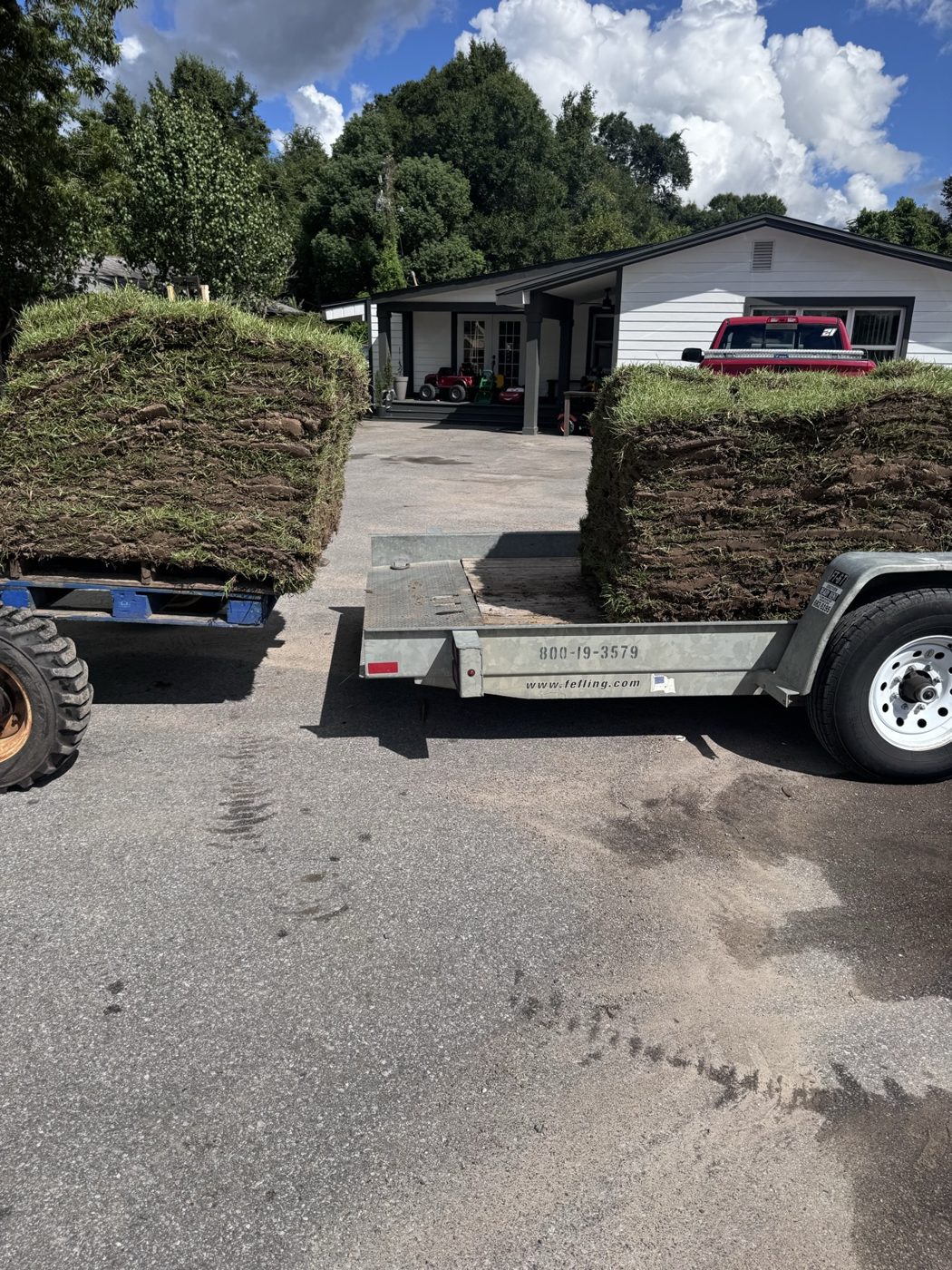 A trailer loaded with pallets of green sod rolls, with a house in the background.